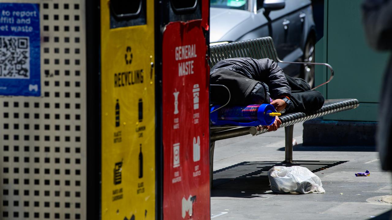 A man sleeping on a bench with a nitrous oxide canister as a pillow