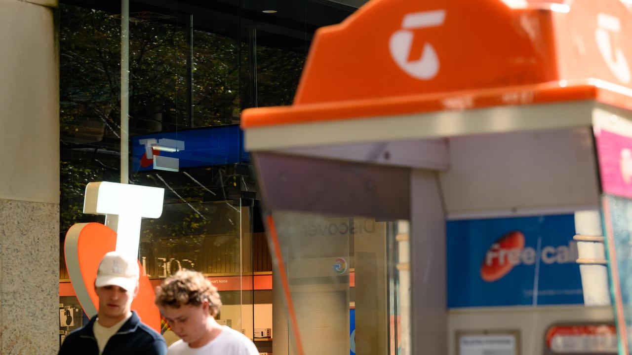 People walk past a Telstra phone booth