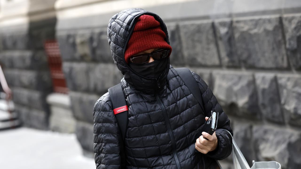 A person in a beanie, hood, sunglasses and face mask walking