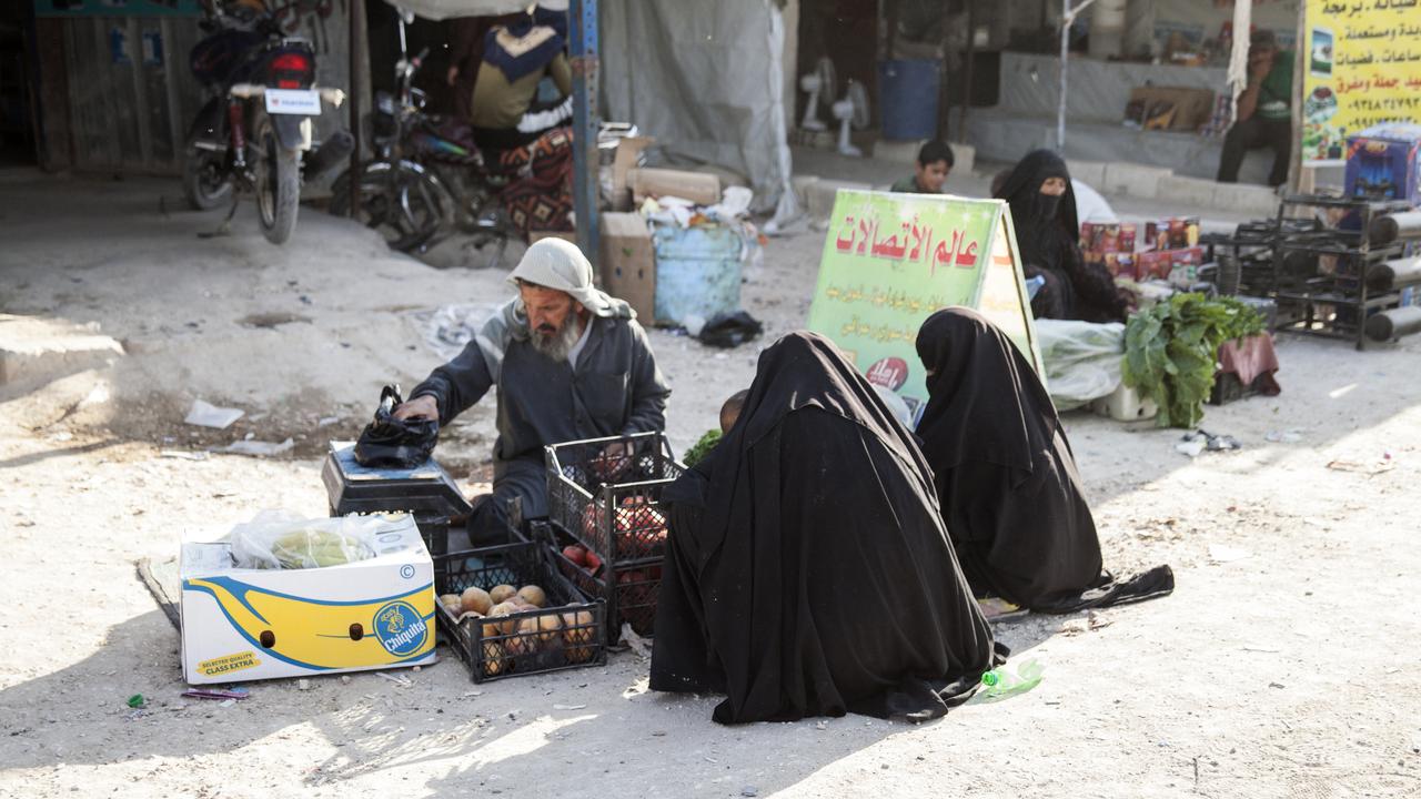 women in full Islamic dress crouch at a marketplace