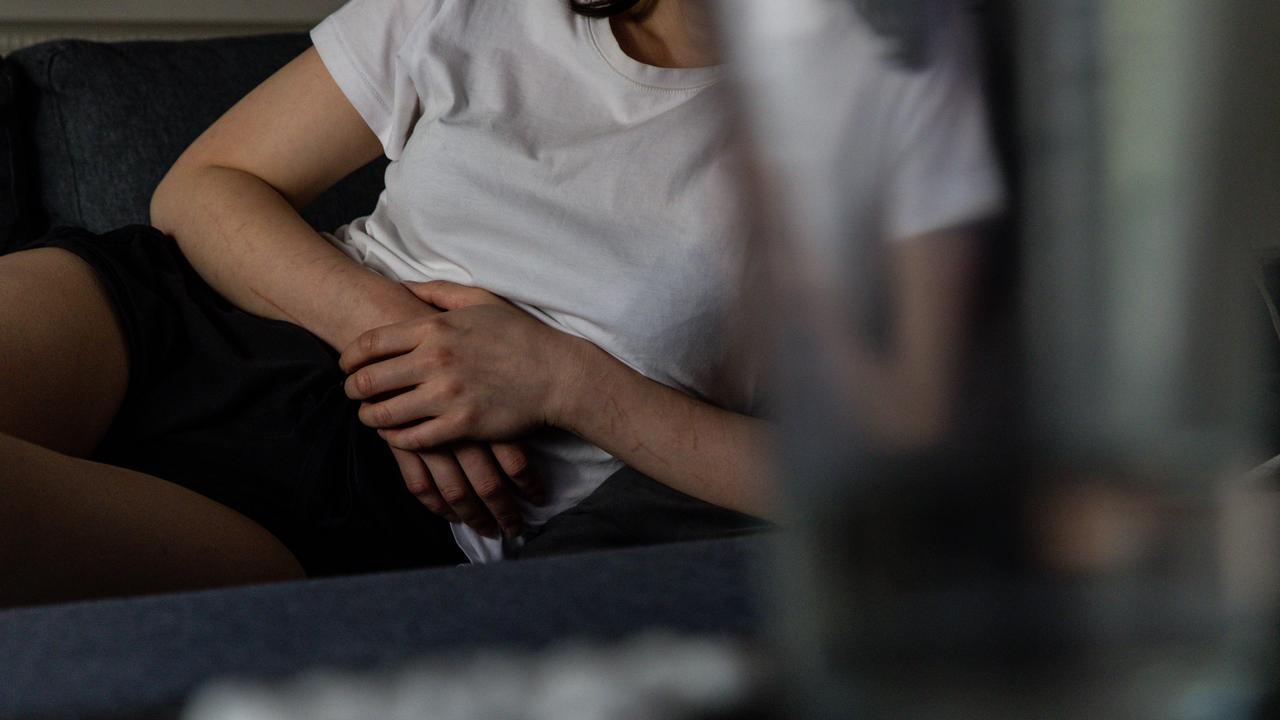 A person holds their stomach as they lie on the couch